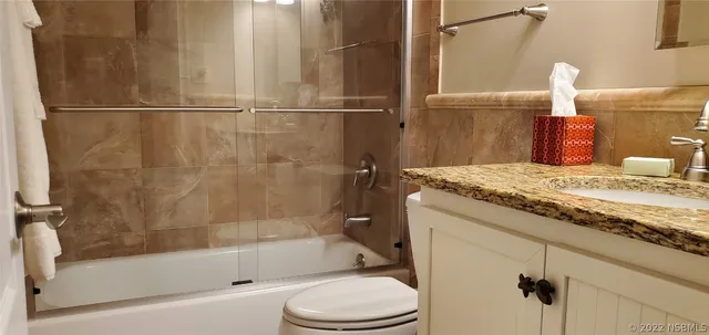 a bathroom with a granite countertop bathtub shower sink vanity and toilet