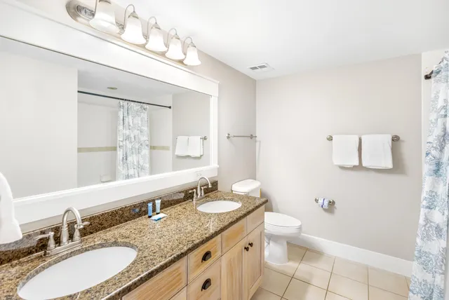 a bathroom with a granite countertop double vanity sink mirror and toilet