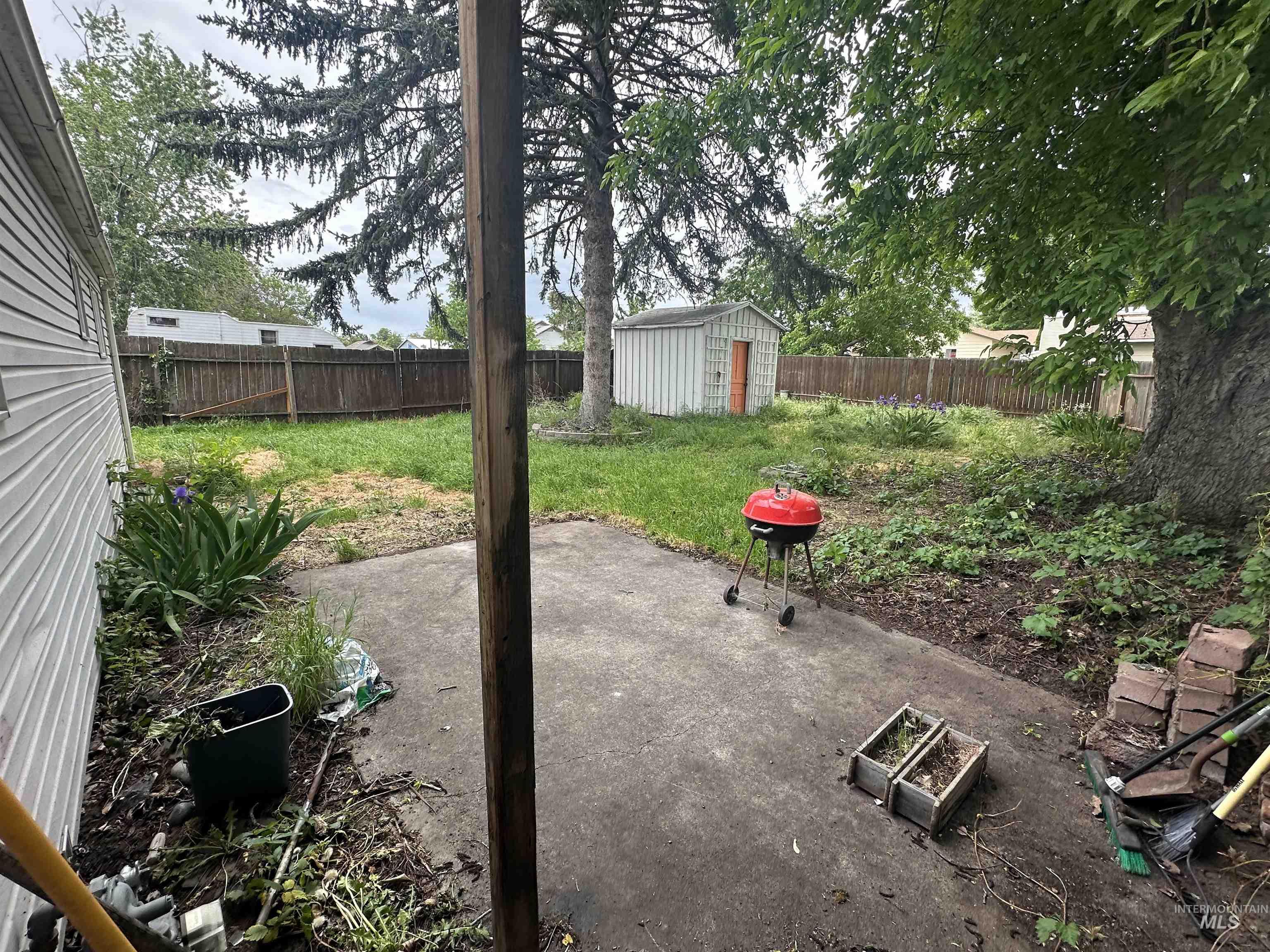 630 Preston Avenue, Unit C Lewiston, ID 83501 - Photo 3 of 10 Concrete patio with a wood privacy fence, featuring a large mature tree and a storage shed