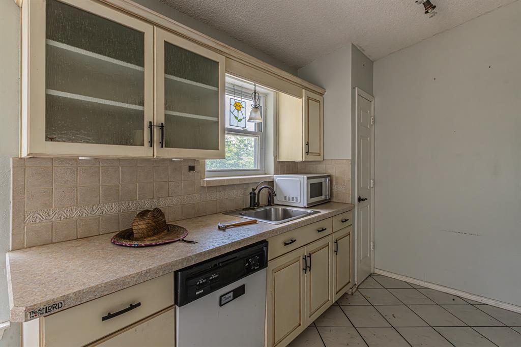 6504 Johnnie Street Watauga, TX 76148 - Photo 6 of 23 Kitchen area featuring a single-basin sink, light-toned cabinetry with glass-front upper cabinets, and a tile backsplash with decorative accents