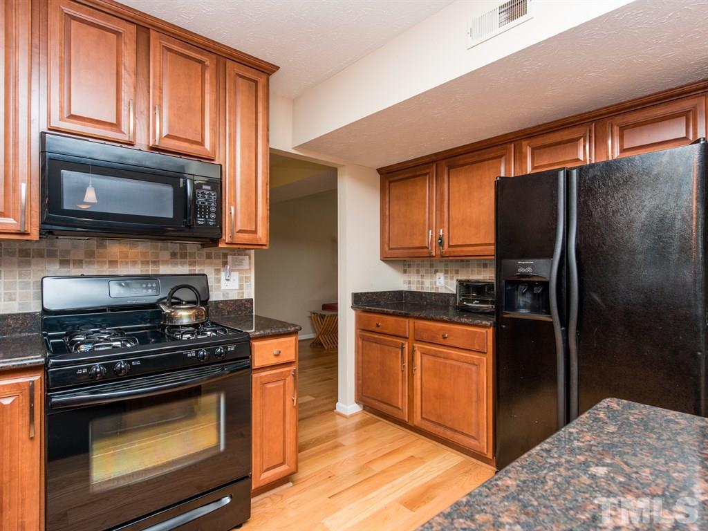 115 Trinity Woods Drive Raleigh, NC 27607 - Photo 4 of 25 a kitchen with granite countertop wooden cabinets a stove top oven a refrigerator and a oven