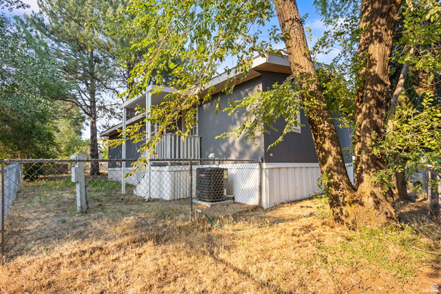 271 Mindella Way Layton, UT 84041 - Photo 25 of 27 Gray exterior with white trim, featuring a partial front porch with vertical railings, a chain-link fence perimeter, and mature trees providing natural shade