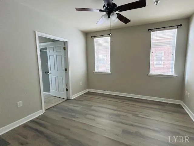 an empty room with wooden floor fan and windows