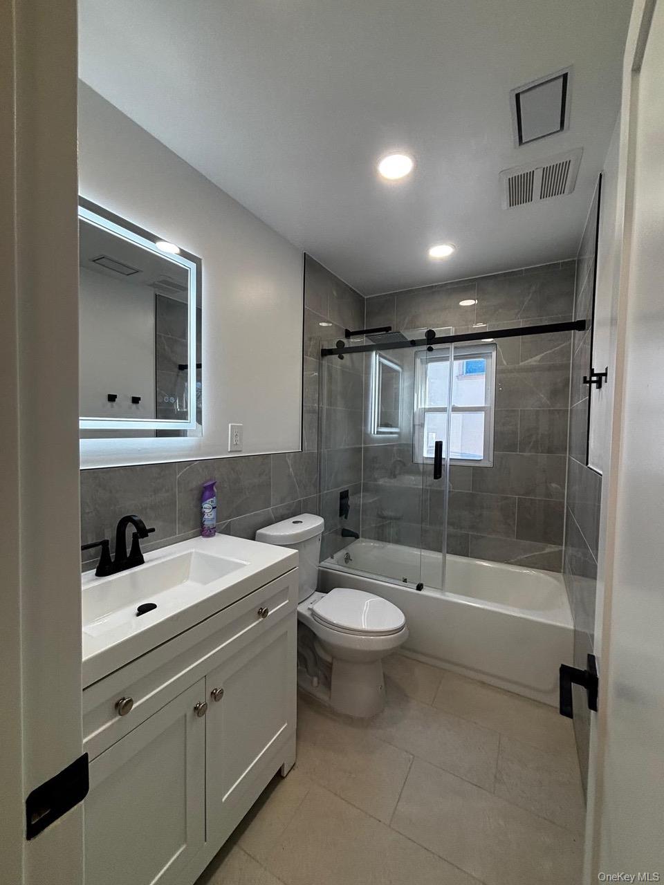 791 Longview Avenue Valley Stream, NY 11581 - Photo 24 of 33 Full bathroom with vanity, shower / bath combination with glass door, tile walls, decorative backsplash, and light tile patterned floors