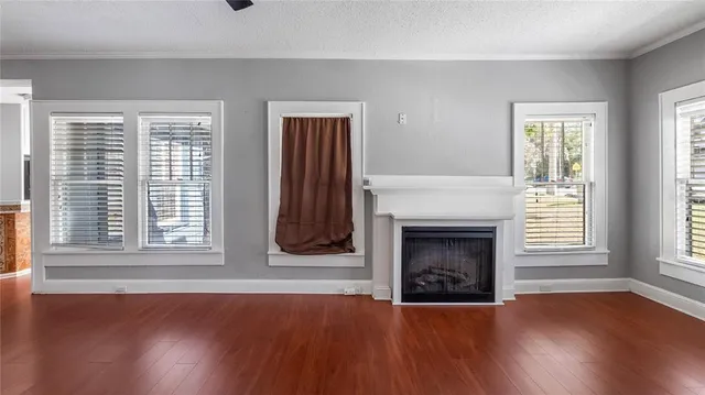 a view of an empty room with wooden floor fireplace and a window