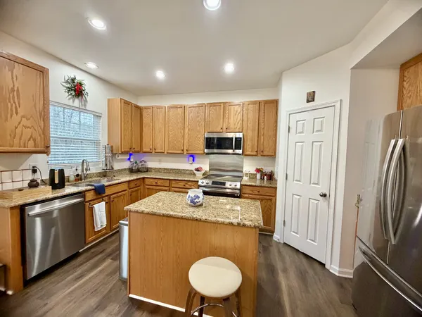 a kitchen with stainless steel appliances granite countertop a refrigerator a stove top oven a sink dishwasher and wooden cabinets with wooden floor