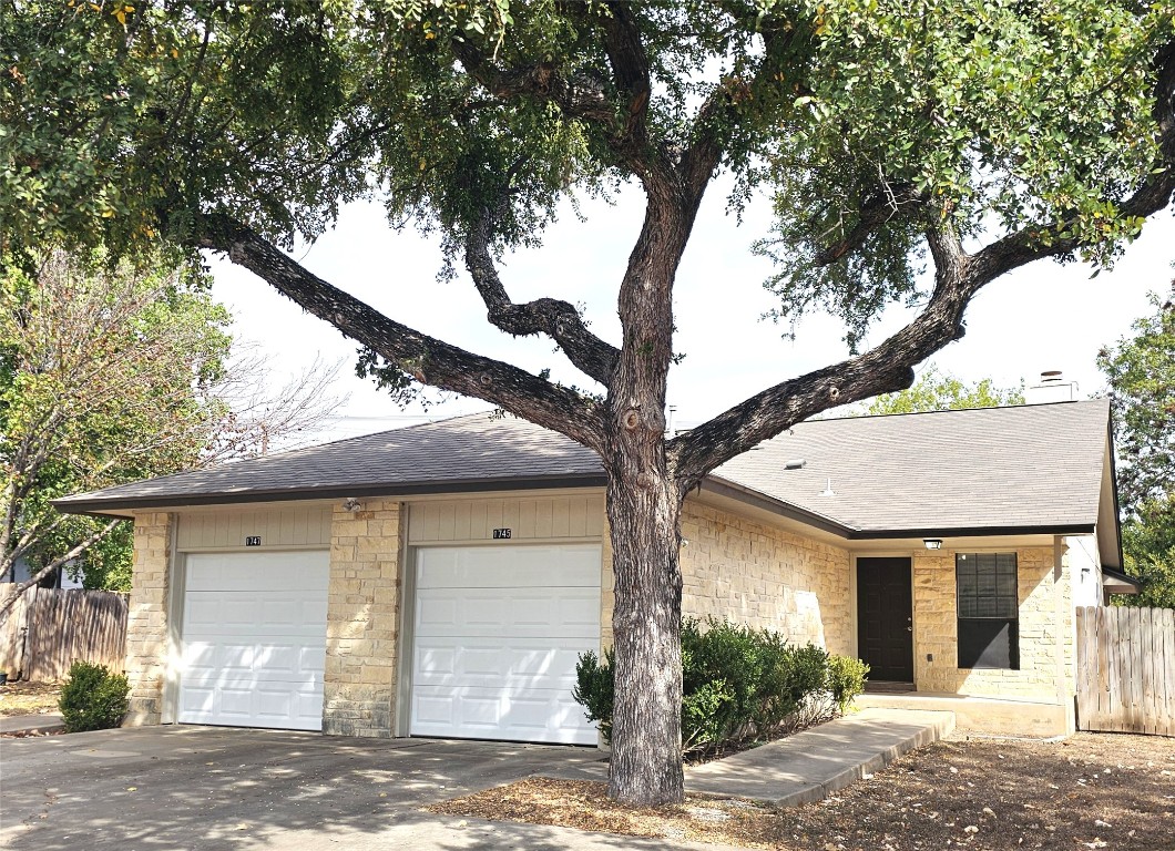 Ranch-style house with stone siding, roof with shingles, driveway, and a chimney