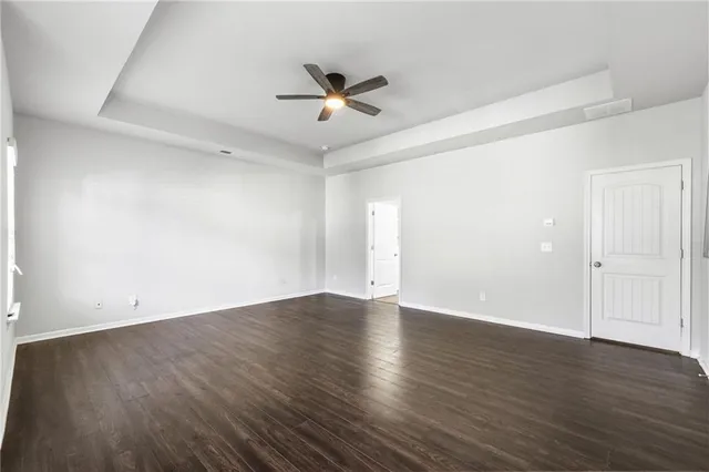 an empty room with wooden floor a ceiling fan and windows