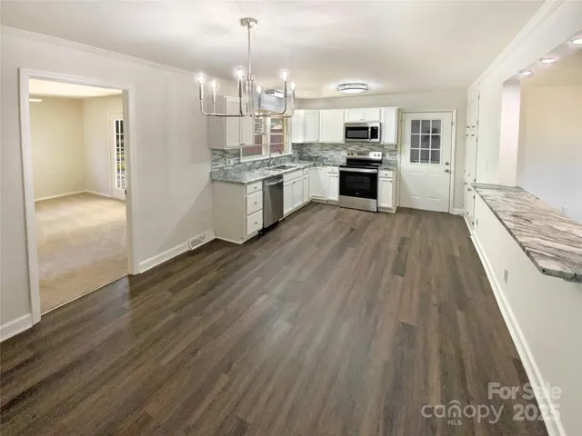 a kitchen with stainless steel appliances granite countertop a stove top oven a sink dishwasher and a refrigerator with wooden floor