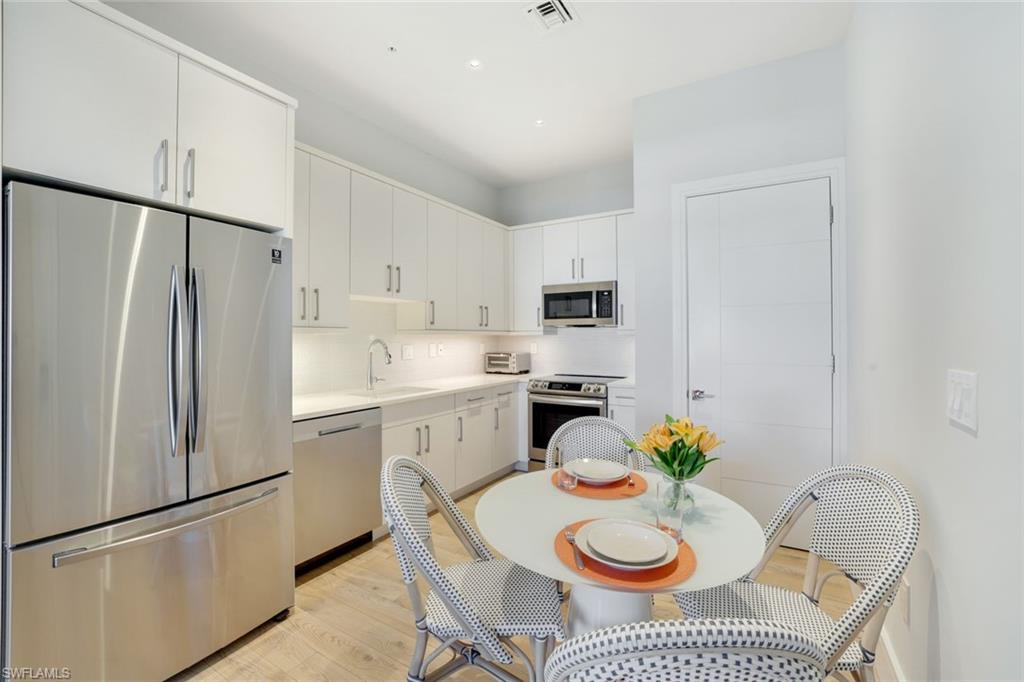 101 8th Street South, Unit 301 Naples, FL 34102 - Photo 5 of 17 a kitchen with stainless steel appliances granite countertop a refrigerator a sink a stove a dining table and chairs with wooden floor
