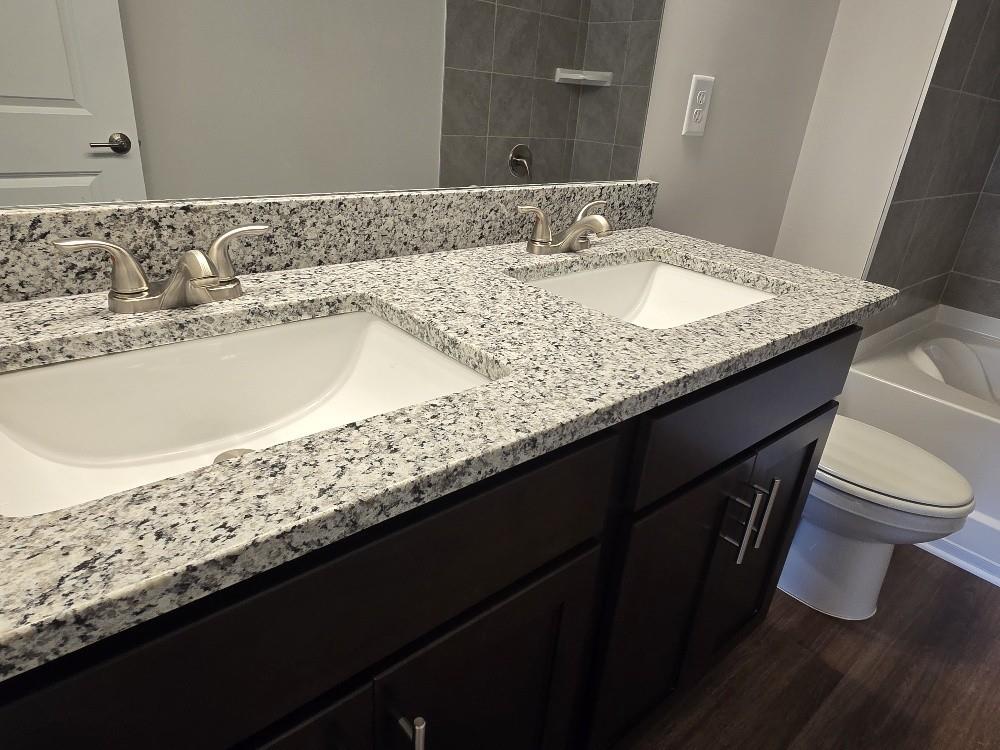 6198 Ripple Way, Unit 87 Atlanta, GA 30349 - Photo 17 of 23 a bathroom with a granite countertop sink a toilet and a mirror