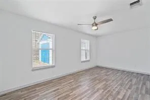 an empty room with wooden floor ceiling fan and windows