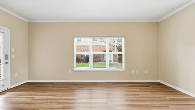 a view of an empty room with wooden floor and a window