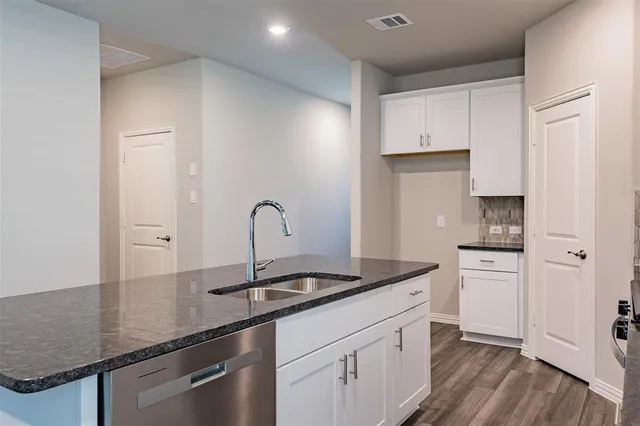 a kitchen with stainless steel appliances granite countertop a sink dishwasher a refrigerator and white cabinets with wooden floor