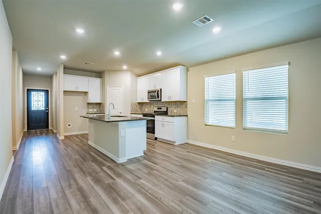 an open kitchen with white cabinets wooden floor and a refrigerator