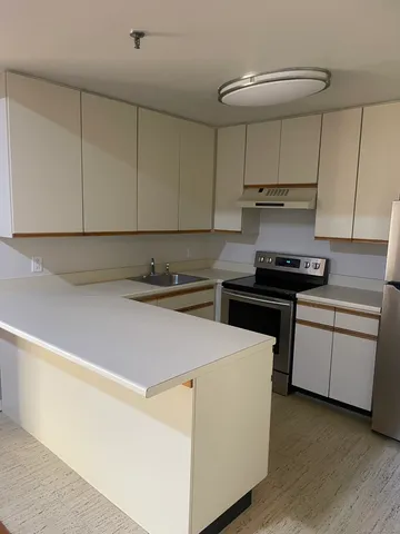 a kitchen with kitchen island granite countertop stainless steel appliances a stove a sink a refrigerator white cabinets and wooden floor