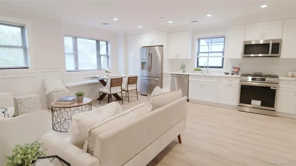 a living room with stainless steel appliances a kitchen island furniture a flat screen tv and a window