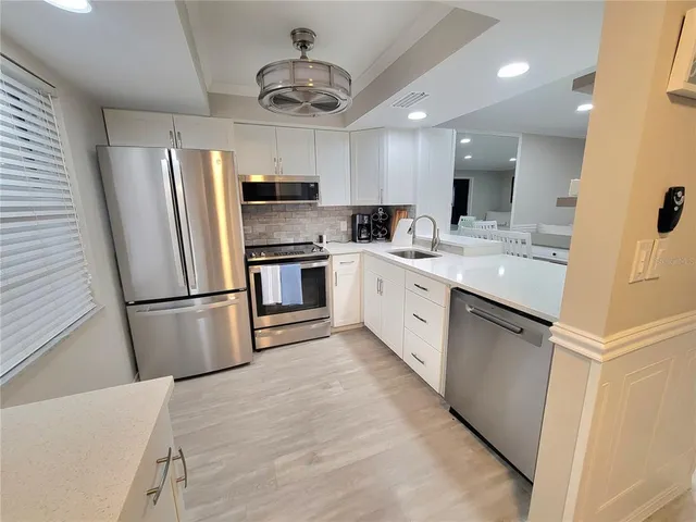 a kitchen with stainless steel appliances granite countertop a refrigerator a stove a sink dishwasher a refrigerator and white cabinets with wooden floor