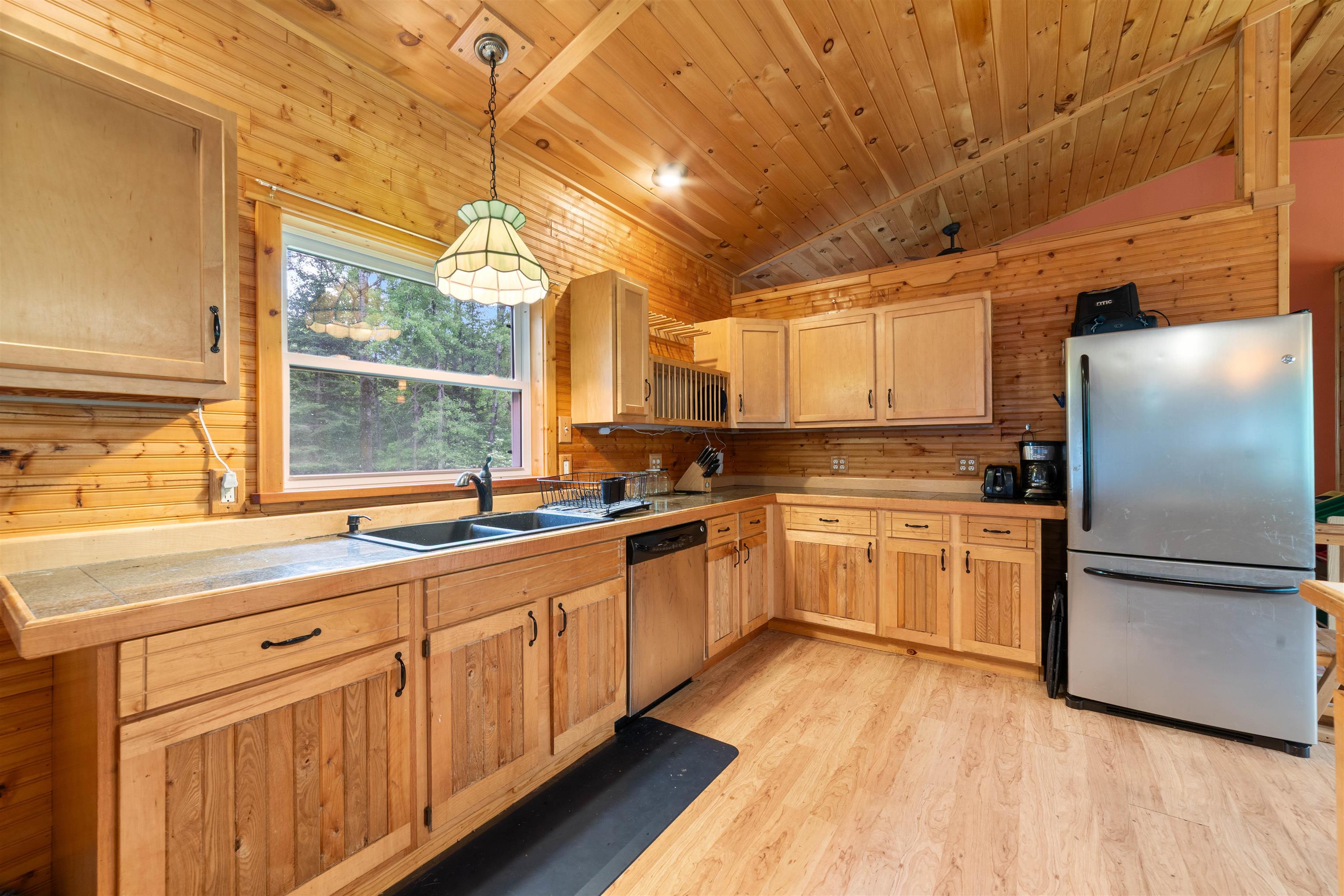 4767 McComber Road Duluth, MN 55803 - Photo 6 of 26 Kitchen featuring appliances with stainless steel finishes, light brown cabinetry, light wood finished floors, wooden walls, and hanging light fixtures