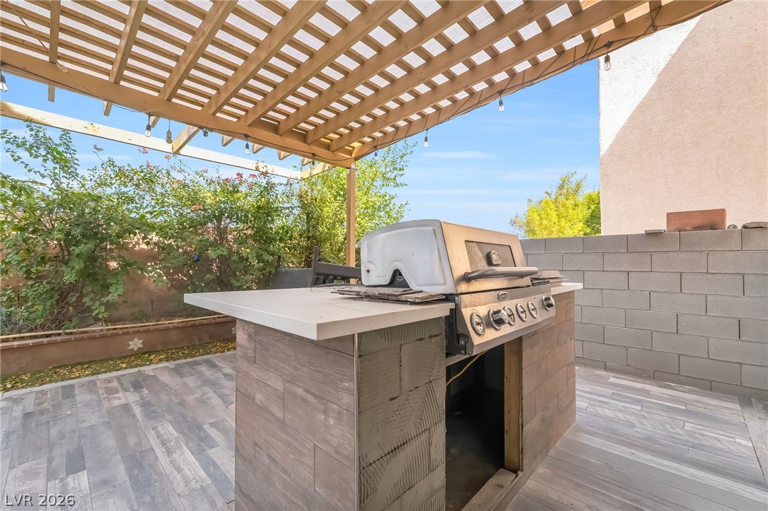 5905 Crumbling Ridge Street Henderson, NV 89011 - Photo 25 of 28 A stone-paved patio area features a built-in outdoor kitchen sheltered by a wood pergola structure.