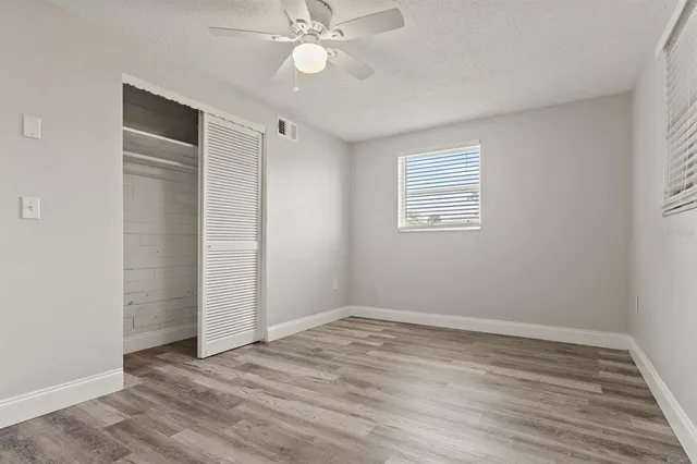 an empty room with wooden floor closet and windows