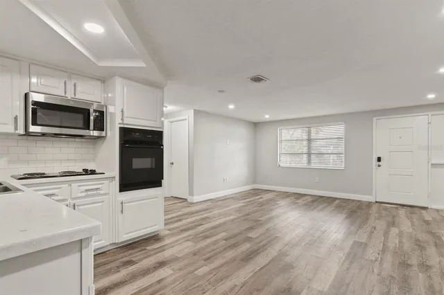 a kitchen with granite countertop a stove a microwave oven a sink dishwasher and white cabinets with wooden floor