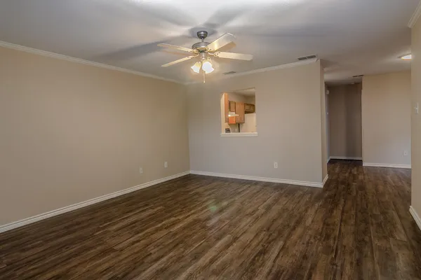 a view of an empty room with wooden floor and a fan