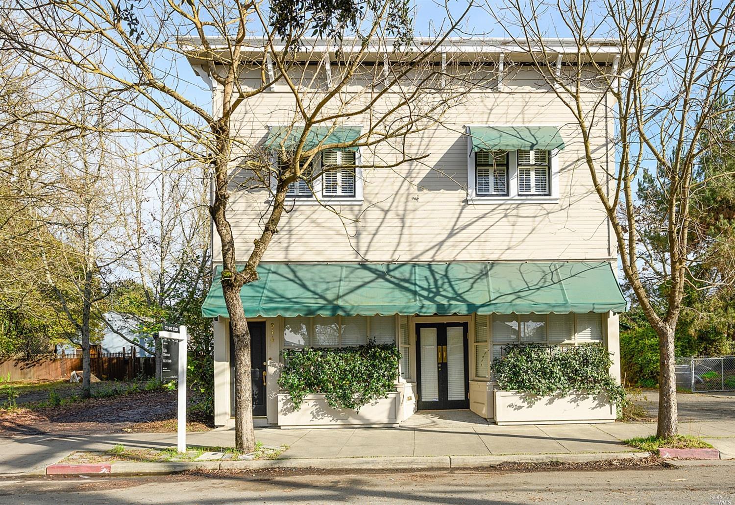 a view of a white house with large tree and wooden fence