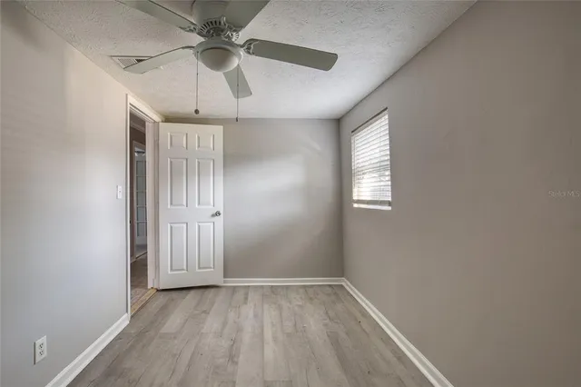 an empty room with wooden floor fan and windows