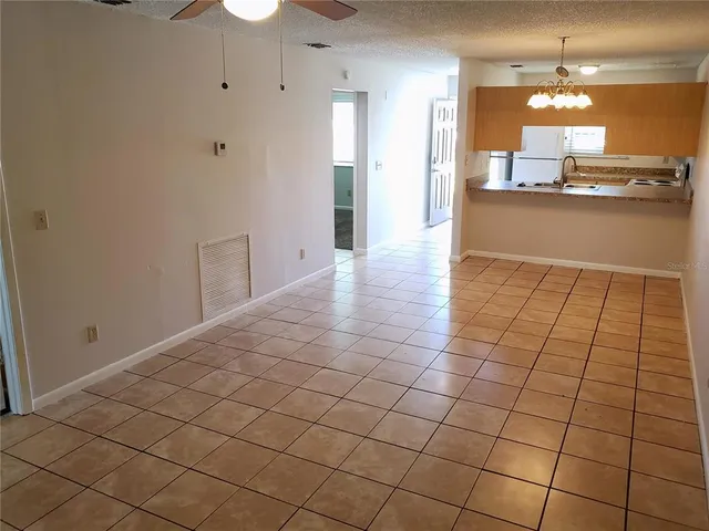 a view of a kitchen and an empty room with a chandelier fan
