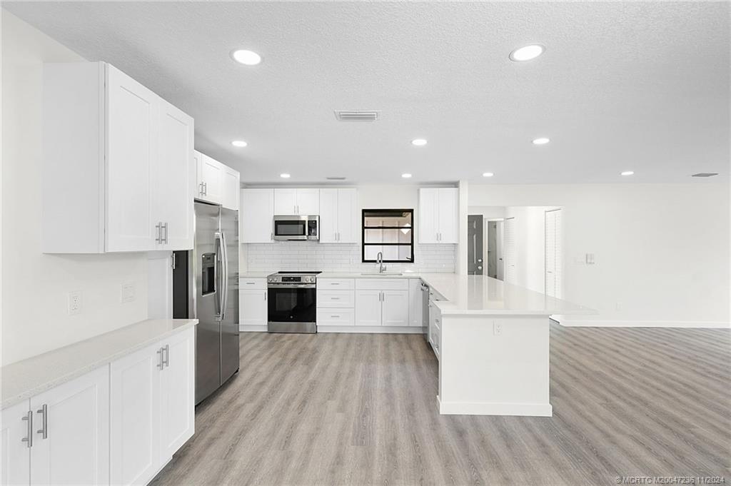 5635 Southeast Miles Grant Road Stuart, FL 34997 - Photo 13 of 73 a large kitchen with stainless steel appliances refrigerator a stove top oven and white cabinets