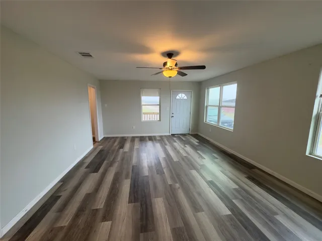 a view of empty room with wooden floor and fan