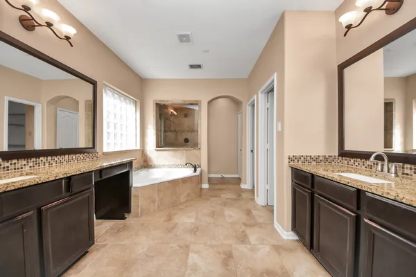 a large bathroom with a granite countertop double vanity sink a mirror and a bathtub