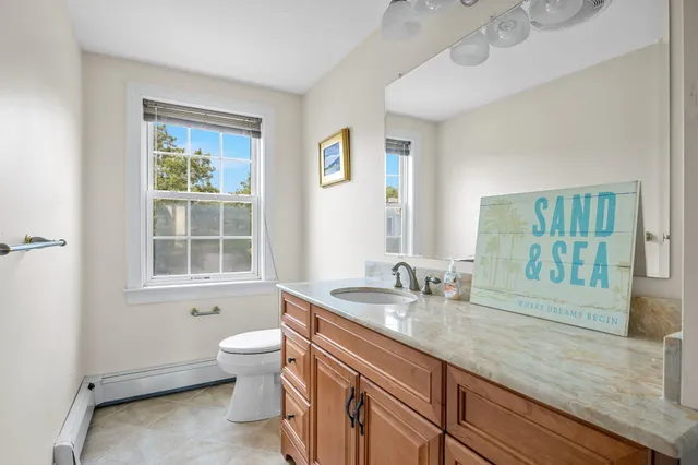 a bathroom with a granite countertop sink a toilet a mirror a window and shower