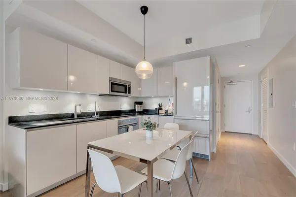 a kitchen with stainless steel appliances granite countertop a sink a stove a microwave a refrigerator white cabinets and wooden floor