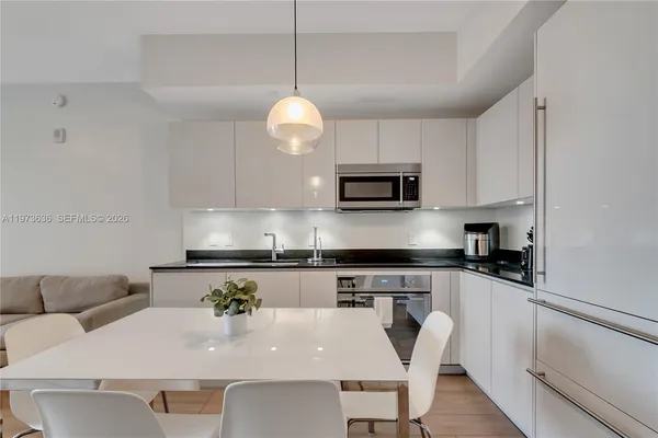 a kitchen with stainless steel appliances granite countertop a stove top oven a sink a dining table and chairs with white cabinets