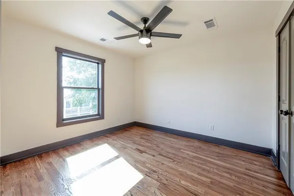 an empty room with wooden floor ceiling fan and windows