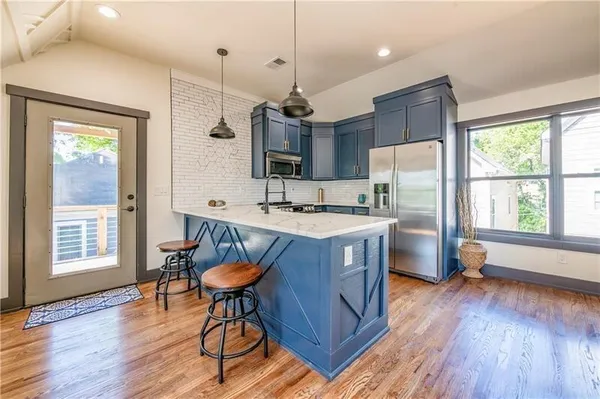 a kitchen with stainless steel appliances granite countertop a refrigerator a sink a stove a dining table and chairs with wooden floor