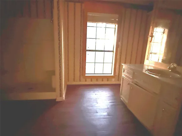 an empty room with wooden floor and windows with curtains