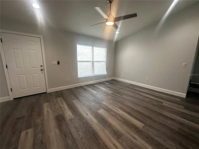 an empty room with wooden floor ceiling fan and windows