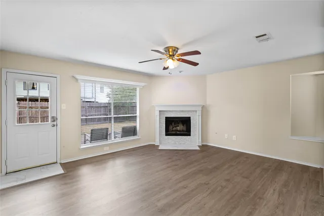 an empty room with wooden floor chandelier fan and windows