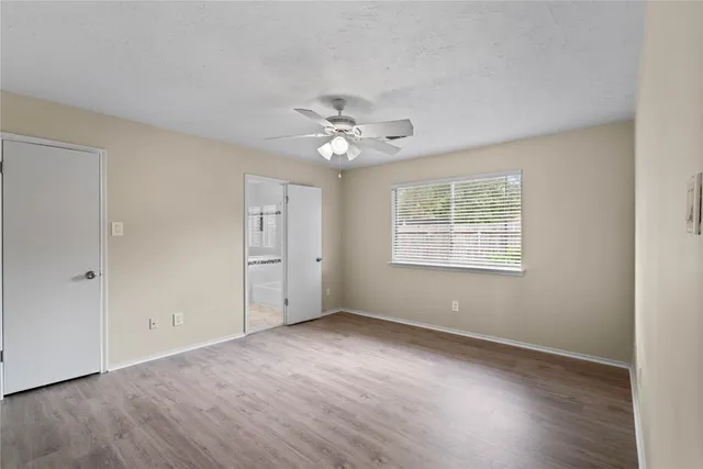 an empty room with wooden floor ceiling fan and window