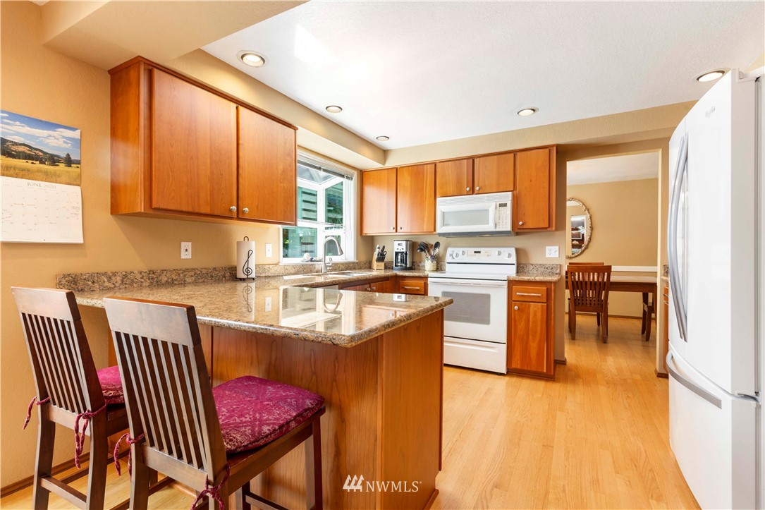 1508 243rd Place Southeast Bothell, WA 98021 - Photo 14 of 32 a kitchen with stainless steel appliances granite countertop a stove top oven a sink a dining table and chairs with wooden floor