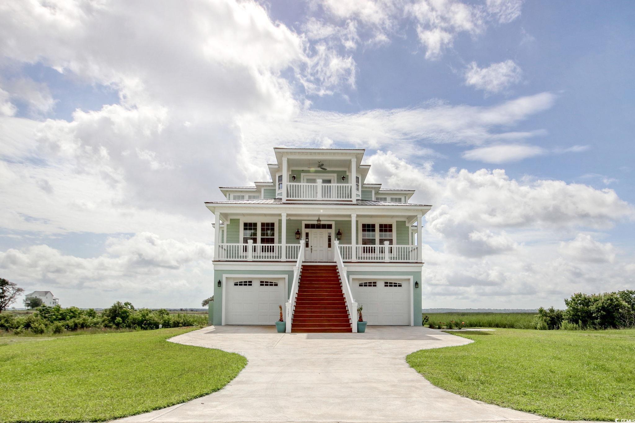 Coastal home with stairway, covered porch, a front lawn, and an attached garage