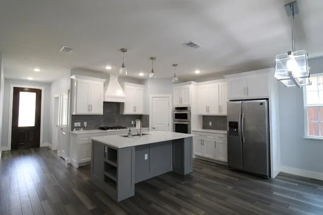 a large kitchen with stainless steel appliances kitchen island a stove a refrigerator a oven and a dining table with wooden floor