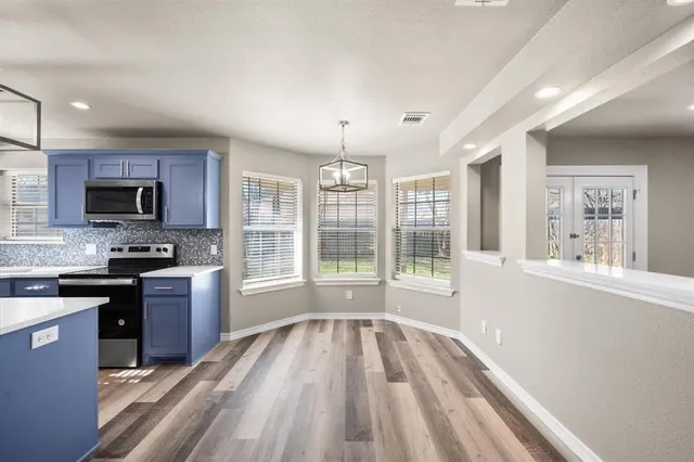 a open kitchen with granite countertop a stove top oven a sink dishwasher a dining table and chairs with wooden floor