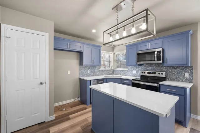 a kitchen with stainless steel appliances granite countertop a sink a stove a microwave oven and a refrigerator with wooden floor