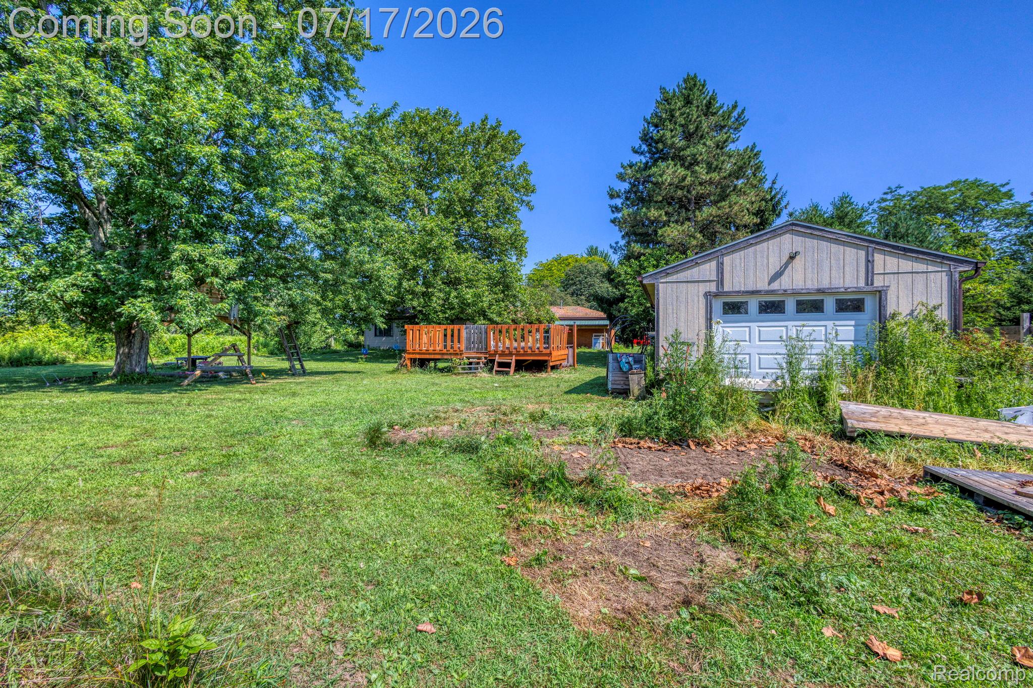 9805 Dolan Road Columbus, MI 48063 - Photo 35 of 39 Spacious property featuring a large detached outbuilding with a garage door, a prominent raised wood deck, and multiple mature trees providing natural shade