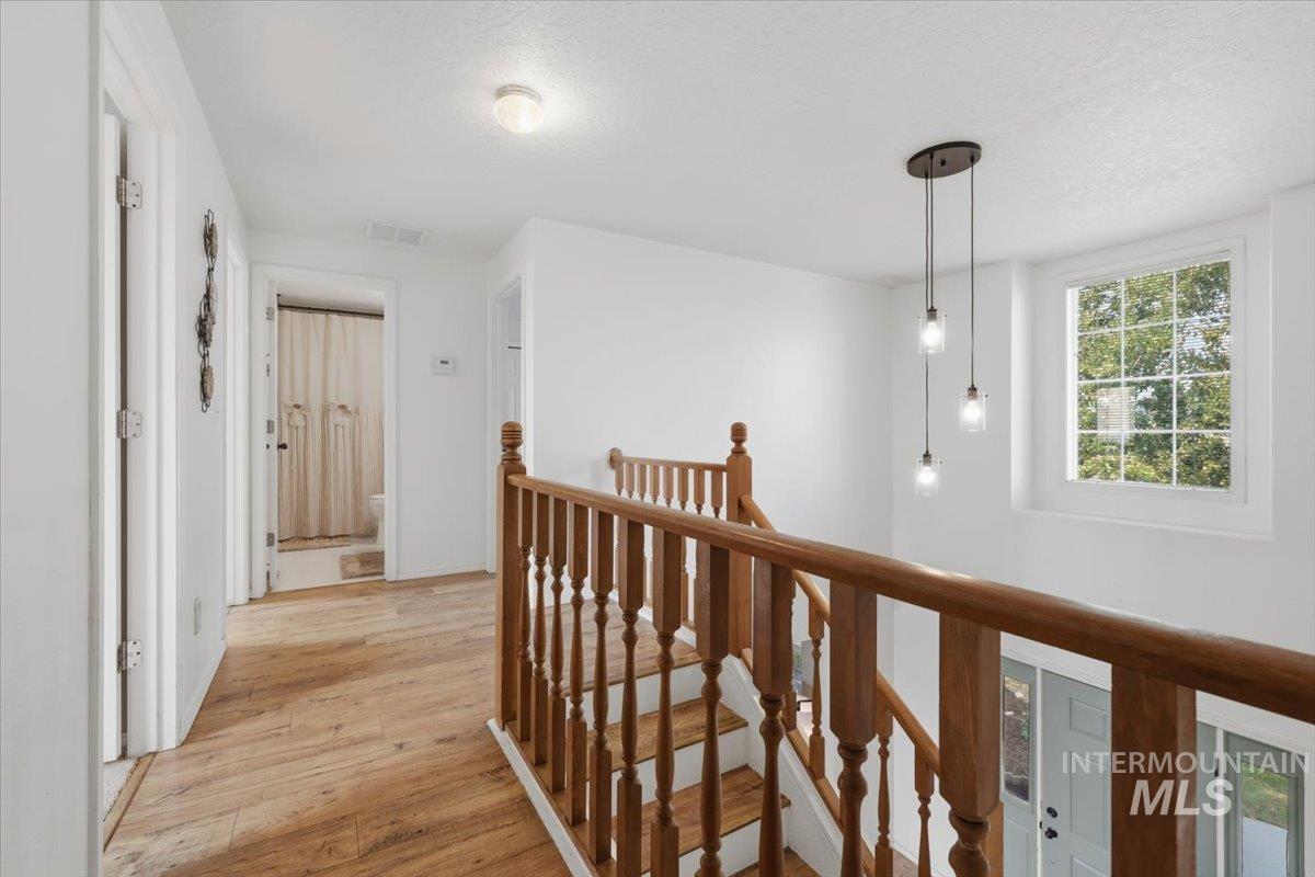 24440 Kenridge Road Caldwell, ID 83607 - Photo 28 of 48 Upper-level landing featuring wood-finish flooring, a wood banister, a multi-bulb pendant light fixture, and a window with natural light