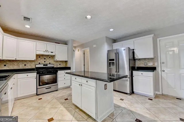 a kitchen with granite countertop a refrigerator sink and white cabinets